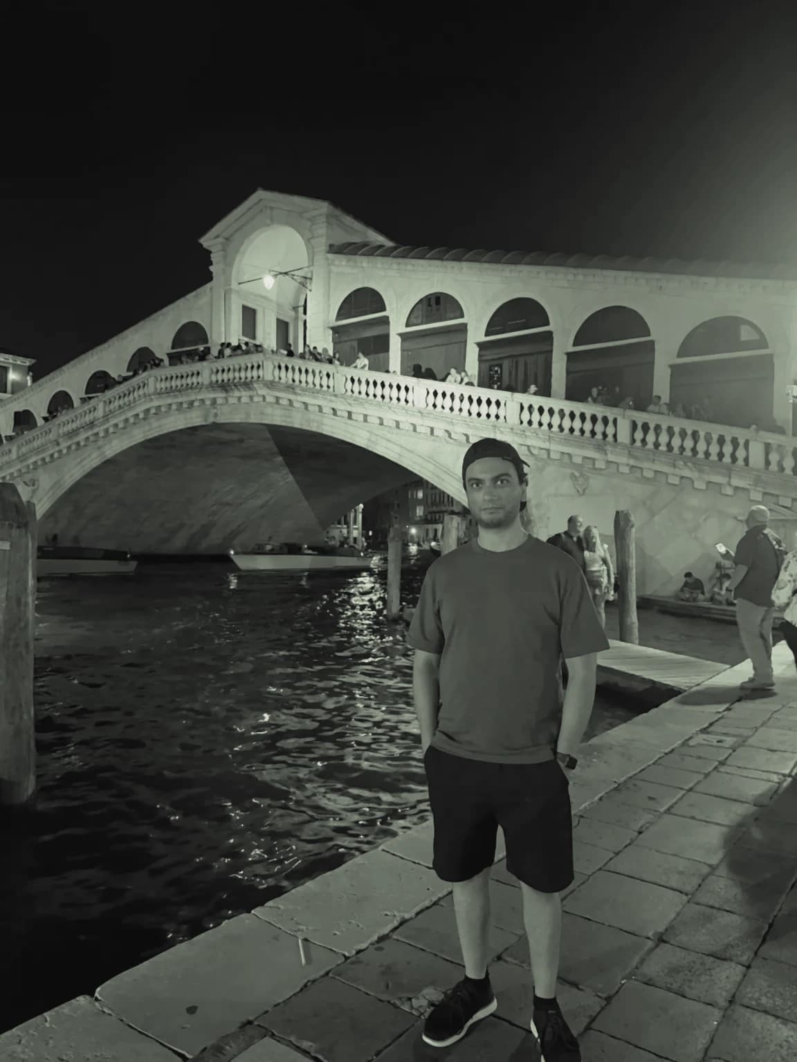 Syed Ibrahim at night on the Grand Canal in Venice, with the Rialto Bridge lit up behind him.